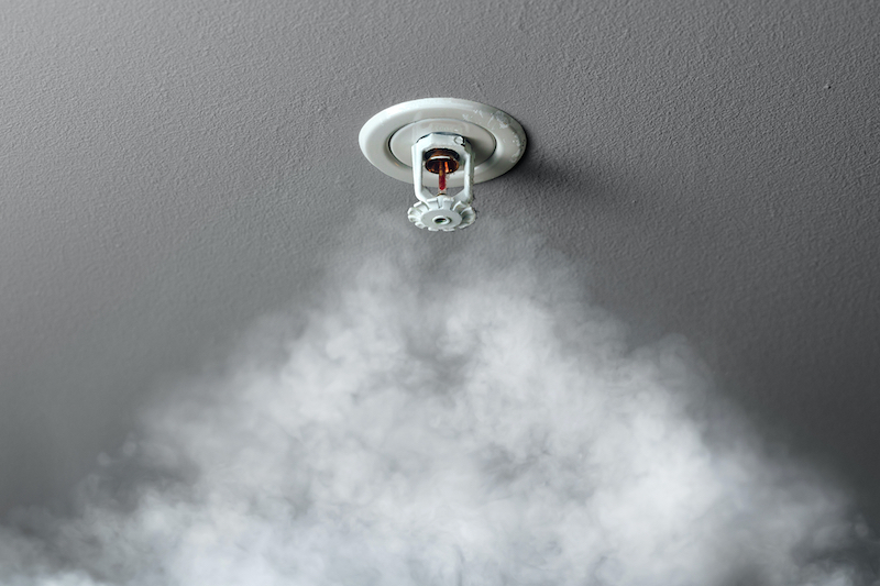 A close up picture of a fire alarm sprinkler system in action with smoke