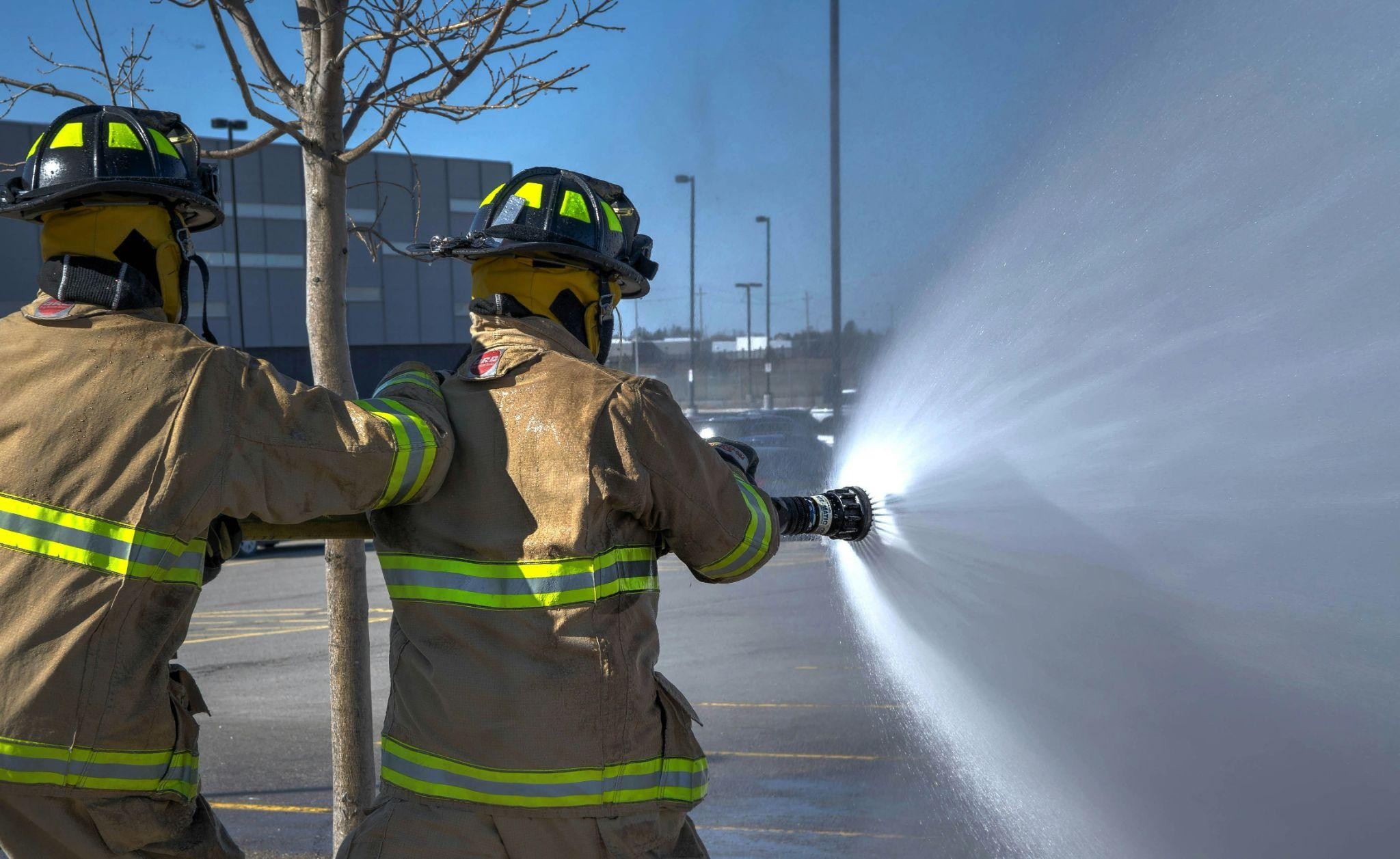 Two firefighters holding a fire hose spraying a powerful blast of water